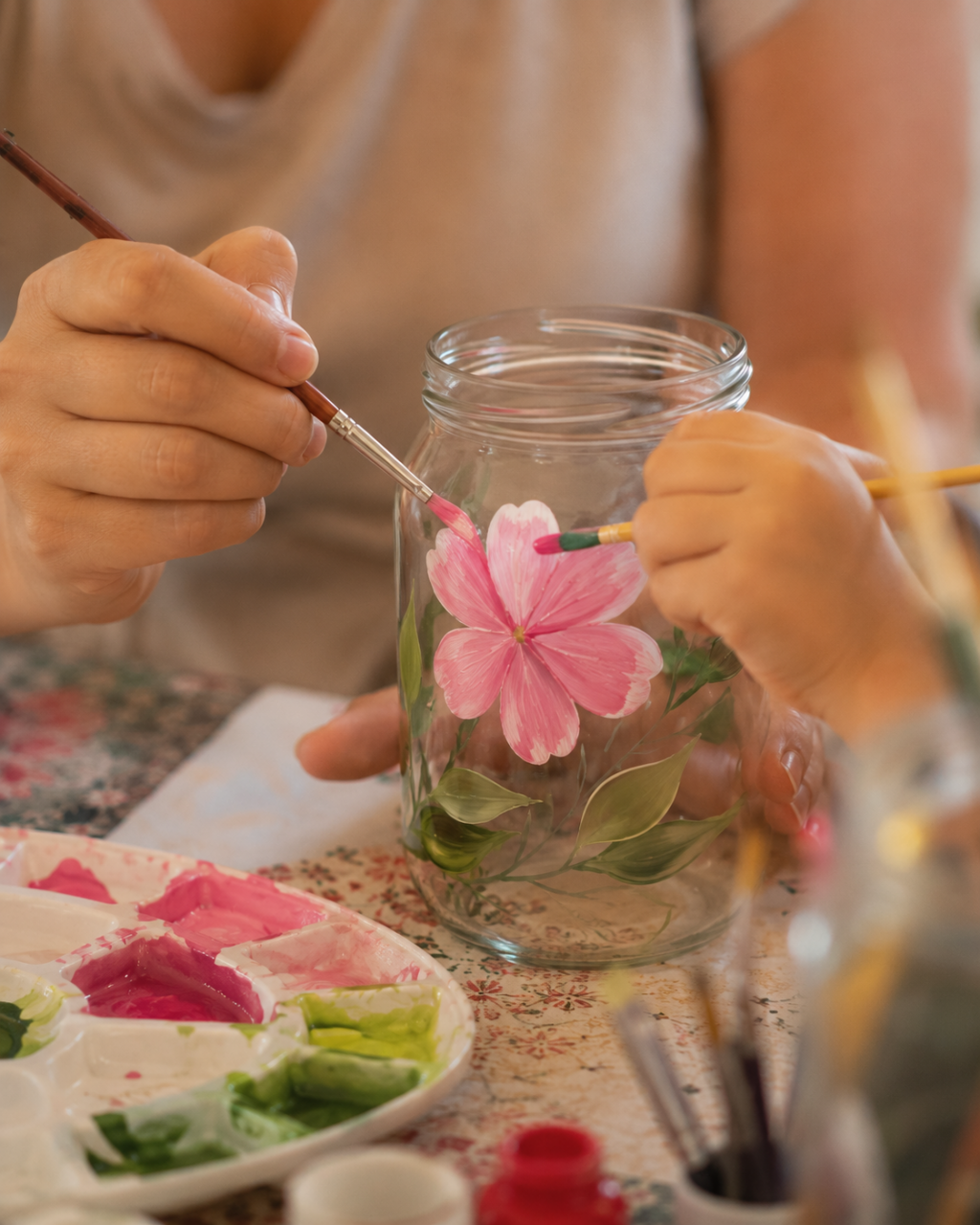 Passo a passo da pintura em vidro: mãos pintando uma flor cor-de-rosa no pote